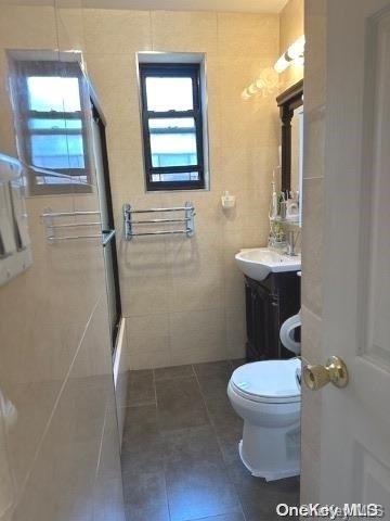 bathroom featuring vanity, toilet, walk in shower, and tile walls