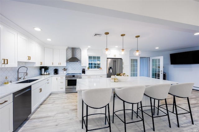 kitchen with appliances with stainless steel finishes, sink, wall chimney range hood, pendant lighting, and a center island