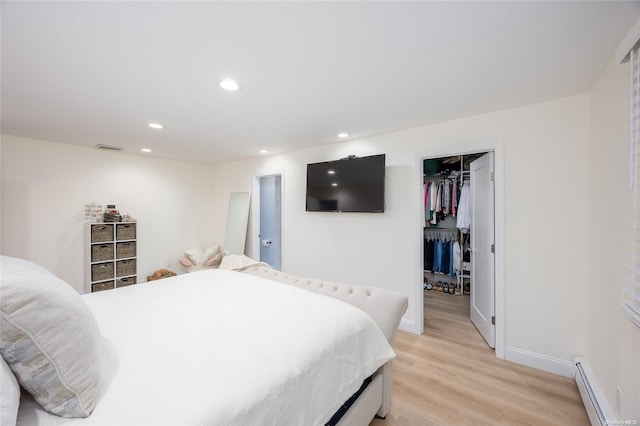 bedroom with light hardwood / wood-style floors, a spacious closet, baseboard heating, and a closet