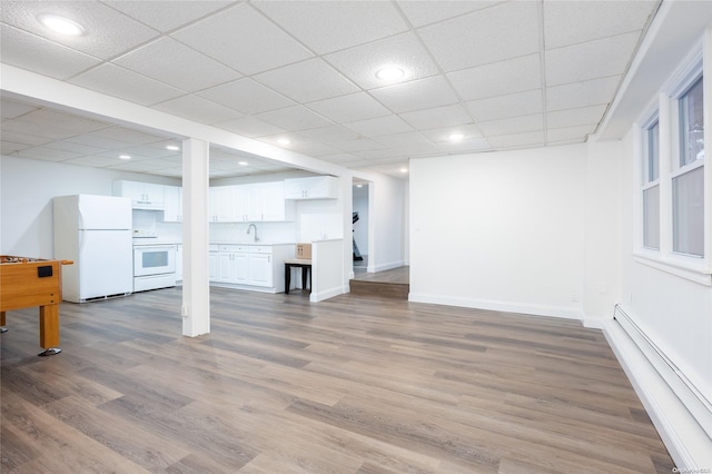 basement featuring a paneled ceiling, baseboard heating, sink, white refrigerator, and hardwood / wood-style floors