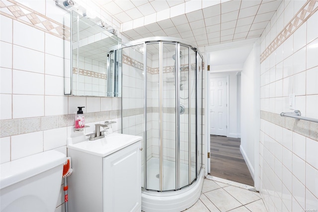 bathroom with hardwood / wood-style floors, vanity, a shower with shower door, and tile walls