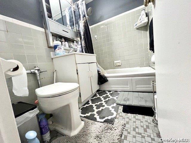 bathroom with shower / bathtub combination with curtain, tile walls, and toilet