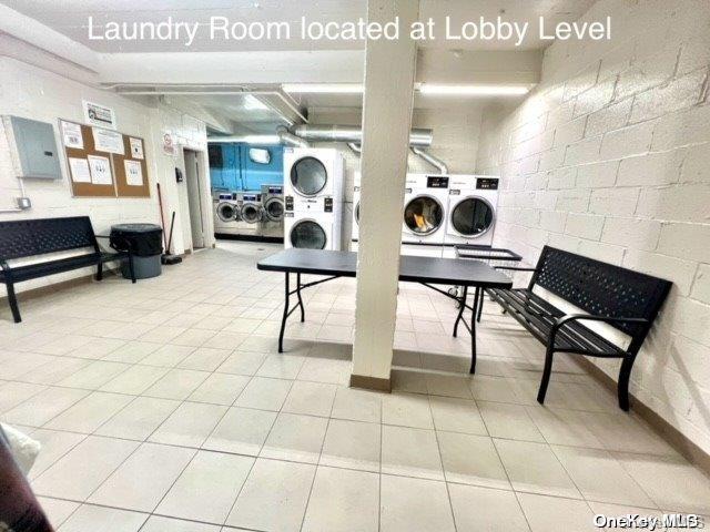 washroom featuring stacked washer / drying machine, washer and dryer, light tile patterned flooring, and electric panel