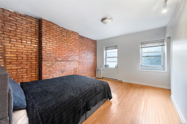 bedroom with radiator heating unit, brick wall, and light wood-type flooring