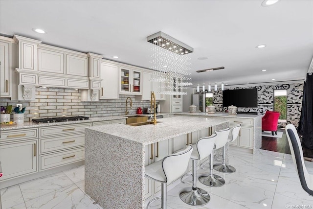 kitchen featuring light stone countertops, backsplash, stainless steel gas cooktop, a kitchen island with sink, and a breakfast bar area