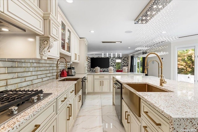 kitchen with light stone countertops, hanging light fixtures, an inviting chandelier, cream cabinetry, and appliances with stainless steel finishes