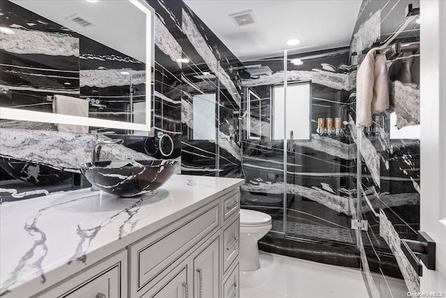 bathroom with vanity, toilet, a shower with door, and tile walls