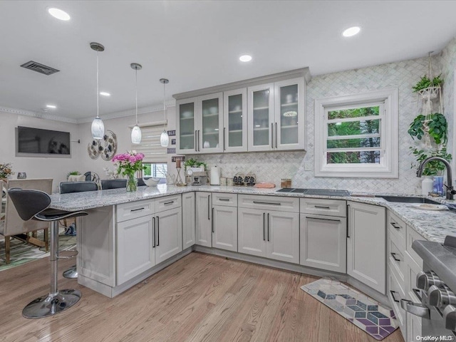 kitchen with a breakfast bar, crown molding, hanging light fixtures, light hardwood / wood-style floors, and light stone counters