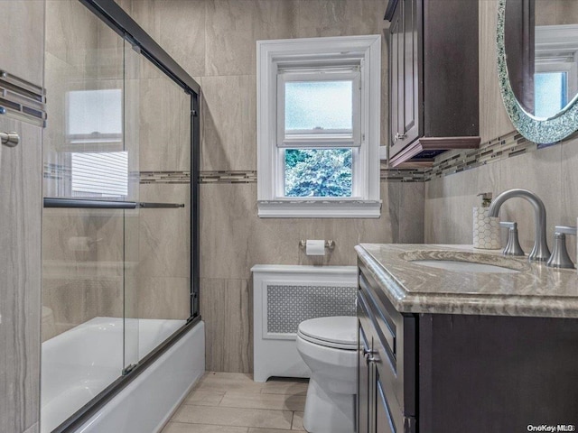 full bathroom with shower / bath combination with glass door, vanity, tile walls, and toilet