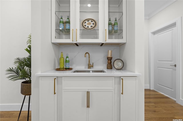 bar with hardwood / wood-style flooring, white cabinetry, ornamental molding, and sink