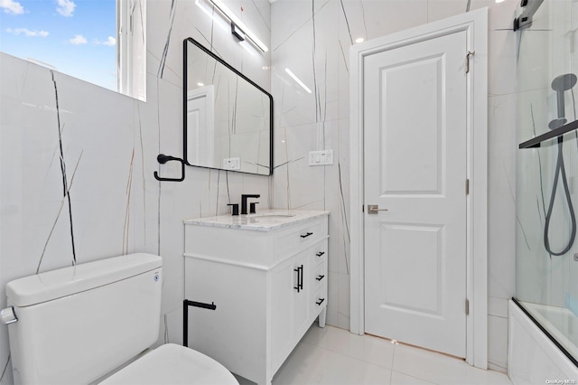 full bathroom with vanity, bath / shower combo with glass door, tile patterned flooring, toilet, and tile walls