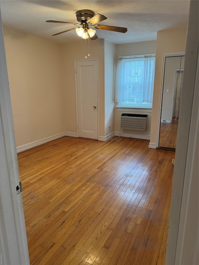 unfurnished room with an AC wall unit, ceiling fan, a textured ceiling, and light wood-type flooring