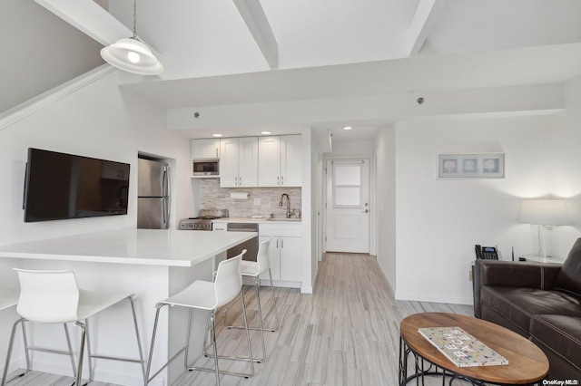 kitchen with stainless steel appliances, sink, white cabinetry, hanging light fixtures, and a breakfast bar area