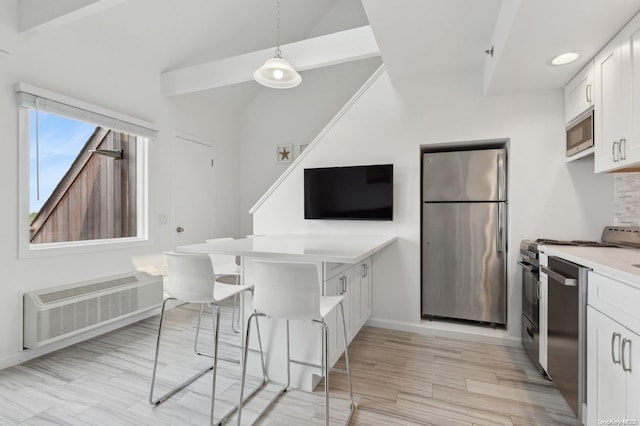 kitchen with stainless steel appliances, decorative light fixtures, an AC wall unit, white cabinets, and light hardwood / wood-style floors