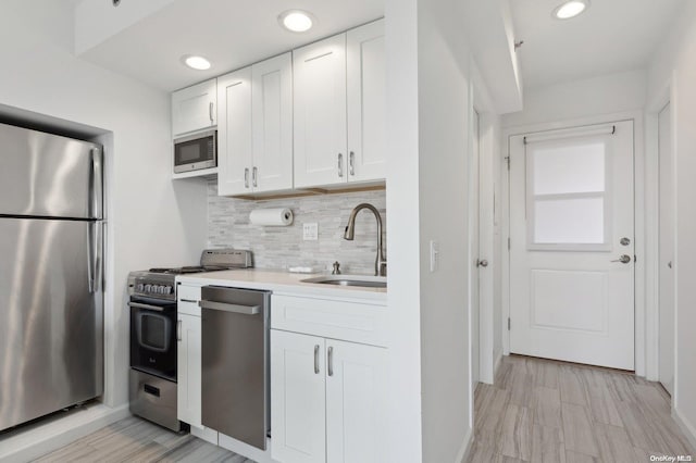 kitchen featuring sink, tasteful backsplash, appliances with stainless steel finishes, white cabinets, and light wood-type flooring