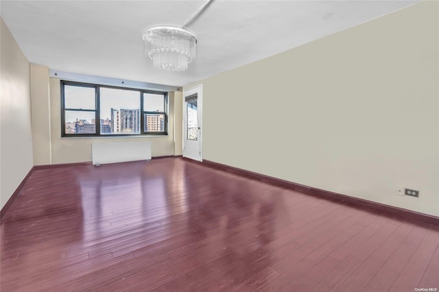 empty room featuring wood-type flooring, radiator heating unit, and a chandelier