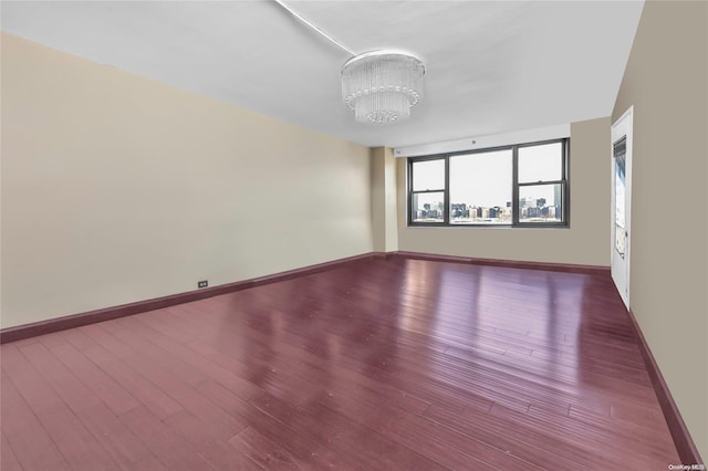 empty room featuring wood-type flooring and an inviting chandelier