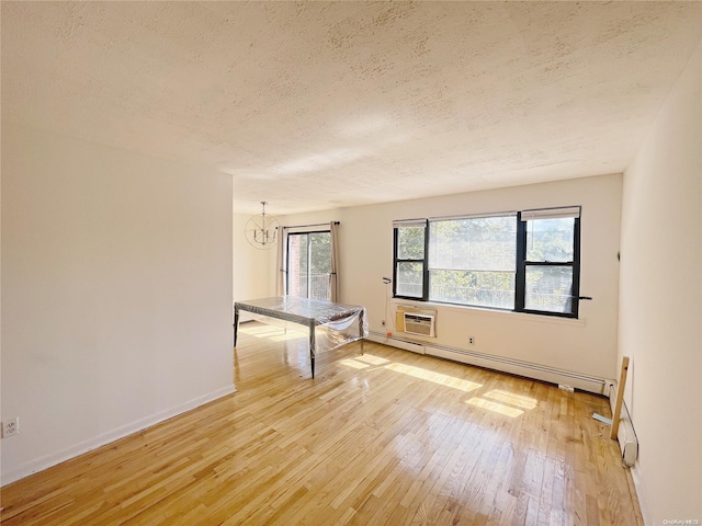 empty room with an inviting chandelier, baseboard heating, a wall mounted AC, light hardwood / wood-style floors, and a textured ceiling