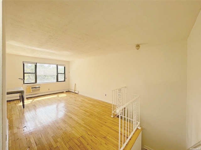 spare room with baseboard heating, a wall unit AC, and wood-type flooring