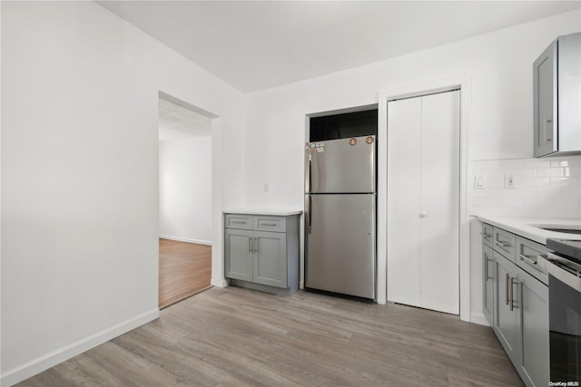 kitchen featuring appliances with stainless steel finishes, backsplash, light hardwood / wood-style floors, and gray cabinetry