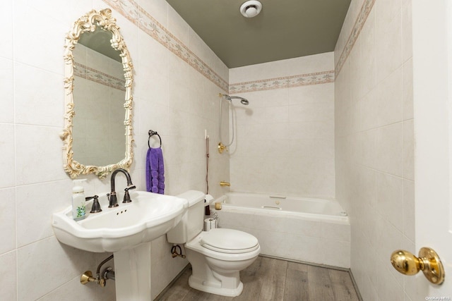 bathroom with tiled shower / bath combo, hardwood / wood-style flooring, toilet, and tile walls