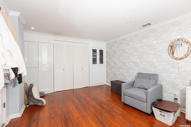 sitting room featuring dark wood-type flooring, ornamental molding, and brick wall