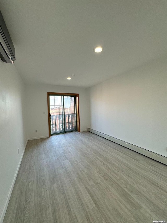 spare room featuring light wood-type flooring, a baseboard radiator, and an AC wall unit