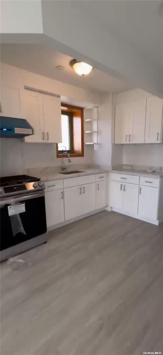 kitchen with stainless steel range, sink, range hood, white cabinets, and light wood-type flooring