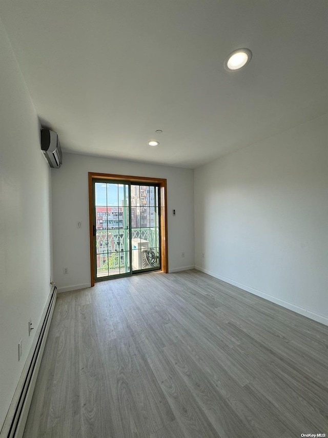 unfurnished room featuring an AC wall unit, light hardwood / wood-style flooring, and a baseboard radiator