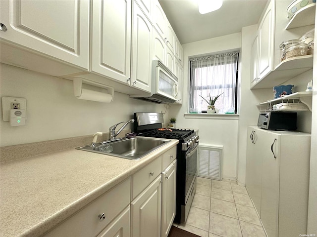 kitchen featuring stainless steel gas range oven, white cabinetry, sink, and light tile patterned floors