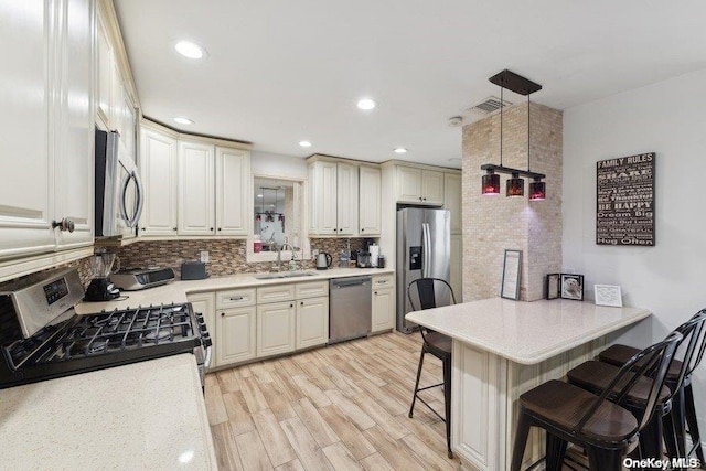 kitchen featuring pendant lighting, a kitchen breakfast bar, sink, light wood-type flooring, and appliances with stainless steel finishes