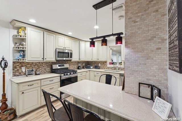 kitchen featuring pendant lighting, a kitchen breakfast bar, sink, appliances with stainless steel finishes, and light hardwood / wood-style floors