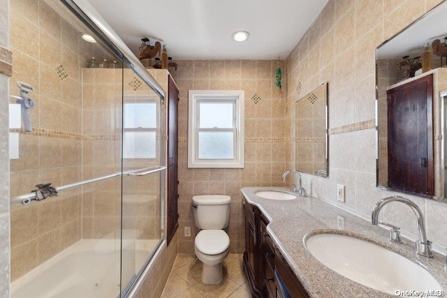 full bathroom featuring tile patterned floors, vanity, shower / bath combination with glass door, tile walls, and toilet