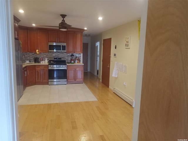 kitchen featuring ceiling fan, baseboard heating, appliances with stainless steel finishes, tasteful backsplash, and light hardwood / wood-style floors