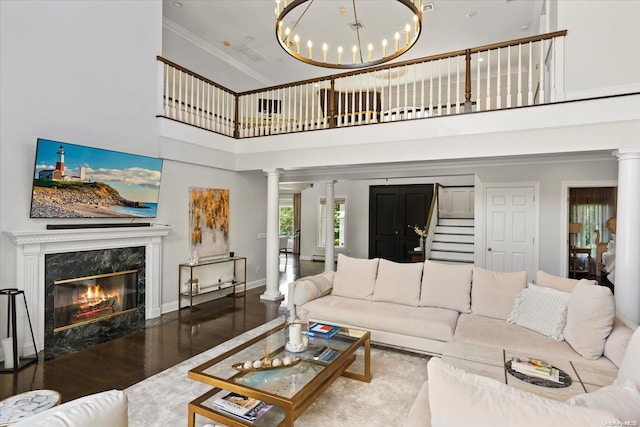 living room with a high end fireplace, crown molding, wood-type flooring, an inviting chandelier, and a high ceiling