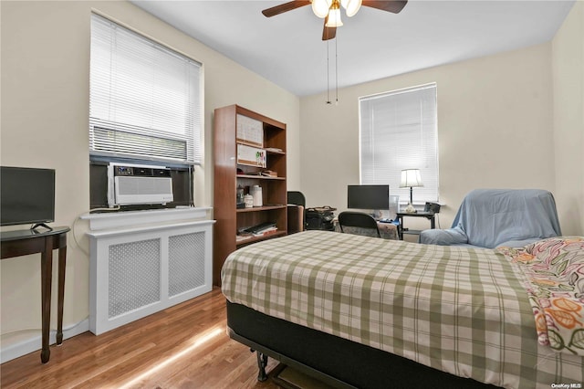 bedroom featuring light hardwood / wood-style flooring, radiator, cooling unit, and ceiling fan