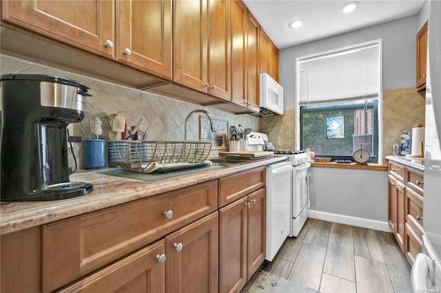 kitchen featuring sink, light stone counters, light hardwood / wood-style floors, white appliances, and decorative backsplash