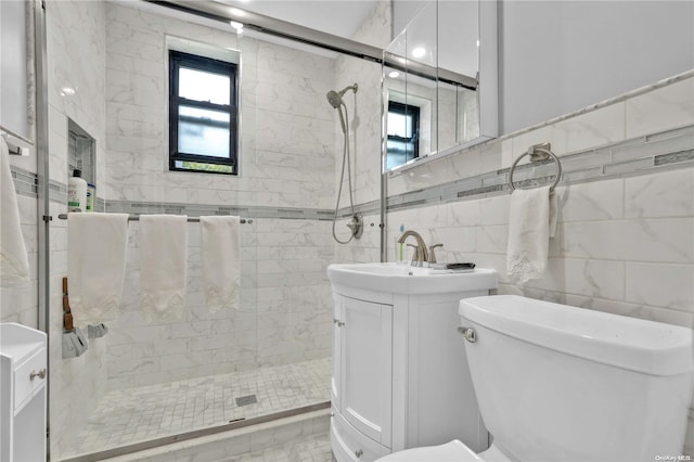 bathroom with vanity, a shower with door, tile patterned floors, toilet, and tile walls