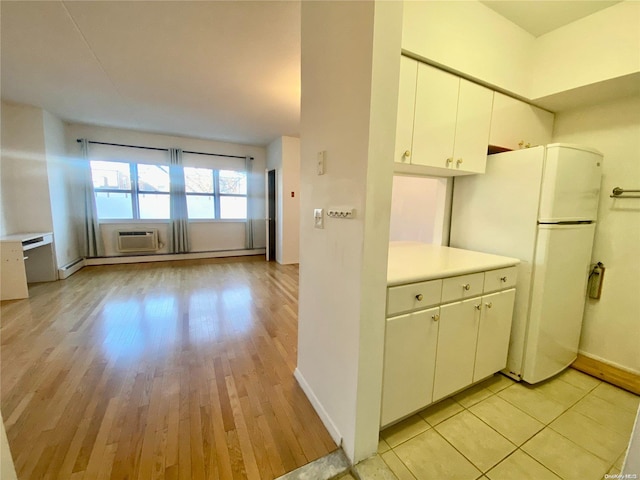 kitchen with white cabinets, white refrigerator, light wood-type flooring, a baseboard radiator, and a wall unit AC