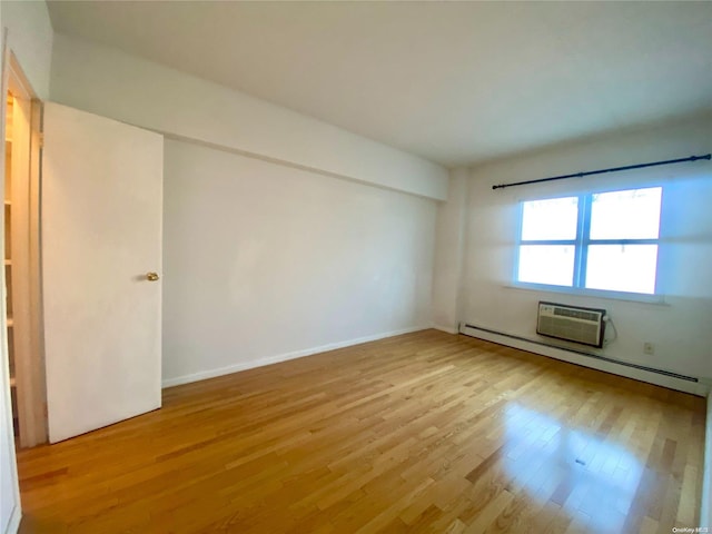 empty room with light hardwood / wood-style floors, a wall unit AC, and a baseboard heating unit