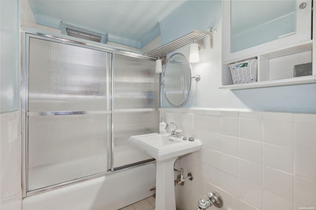 bathroom with combined bath / shower with glass door, tile patterned floors, and tile walls