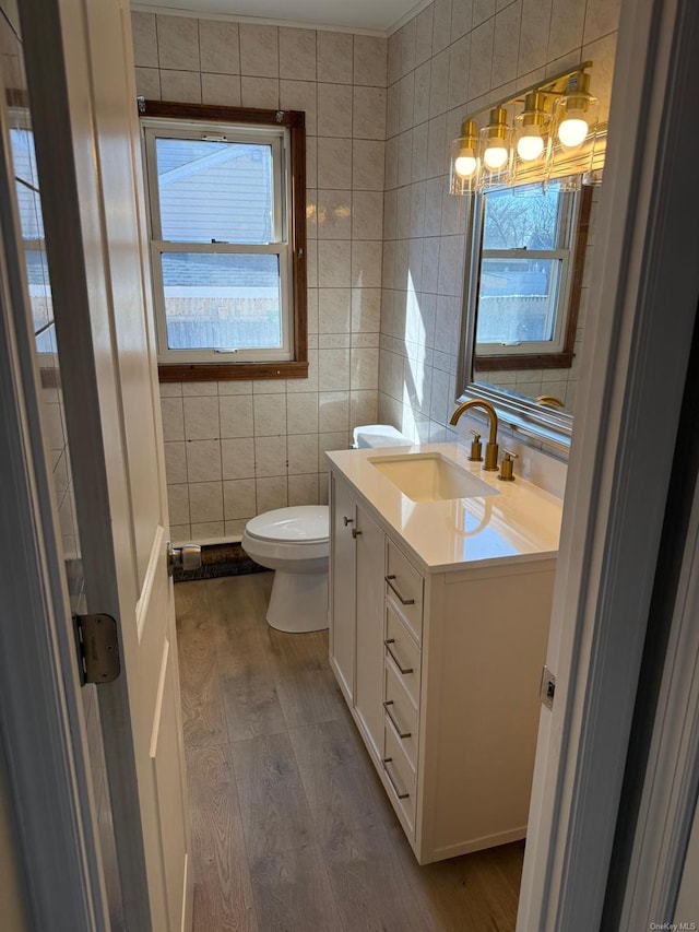 half bath featuring toilet, wood finished floors, vanity, a healthy amount of sunlight, and tile walls