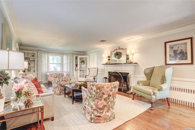 living room featuring built in features, radiator heating unit, light hardwood / wood-style flooring, and crown molding