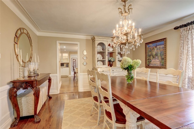 122 Roxen Rd, Rockville Centre, NY 11570 - dining room with light wood finished floors, a decorative wall, a chandelier, wainscoting, and crown molding