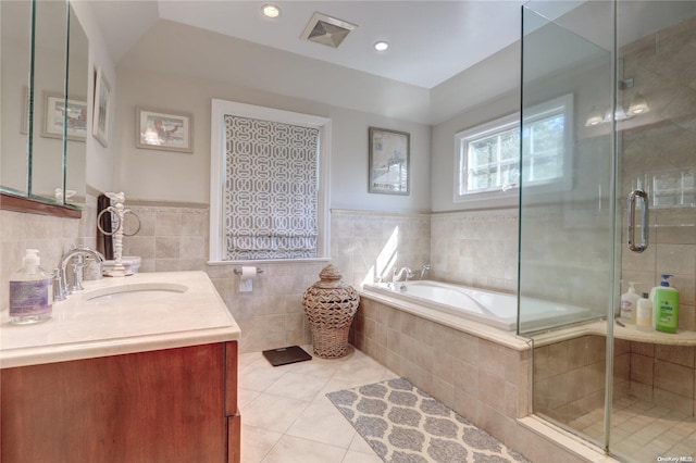 bathroom with tile patterned flooring, vanity, tile walls, and plus walk in shower