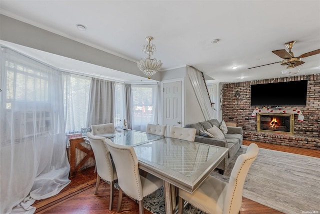 dining room featuring ceiling fan, crown molding, wood-type flooring, and a brick fireplace