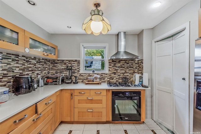 kitchen featuring tasteful backsplash, wall chimney exhaust hood, stainless steel gas cooktop, black oven, and light tile patterned flooring