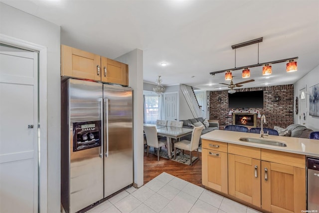 kitchen featuring ceiling fan, sink, stainless steel appliances, a brick fireplace, and light wood-type flooring