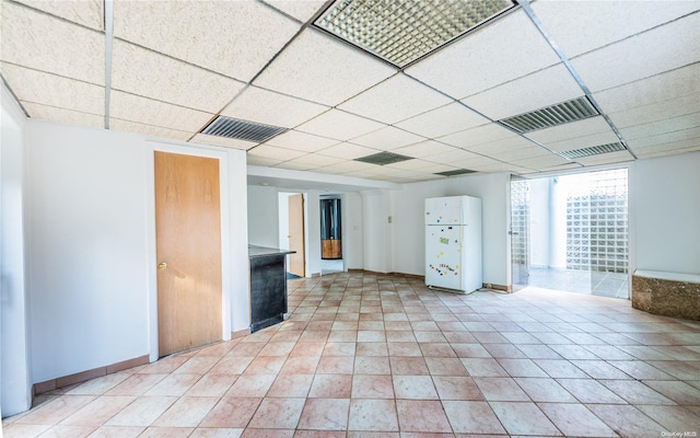 basement with white fridge and a drop ceiling