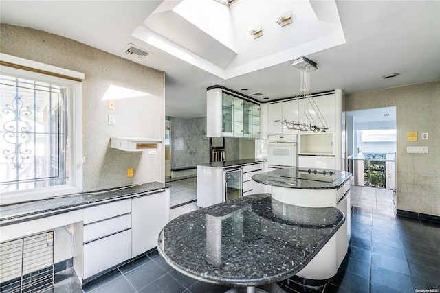 kitchen featuring pendant lighting, white oven, a raised ceiling, a kitchen island, and white cabinetry